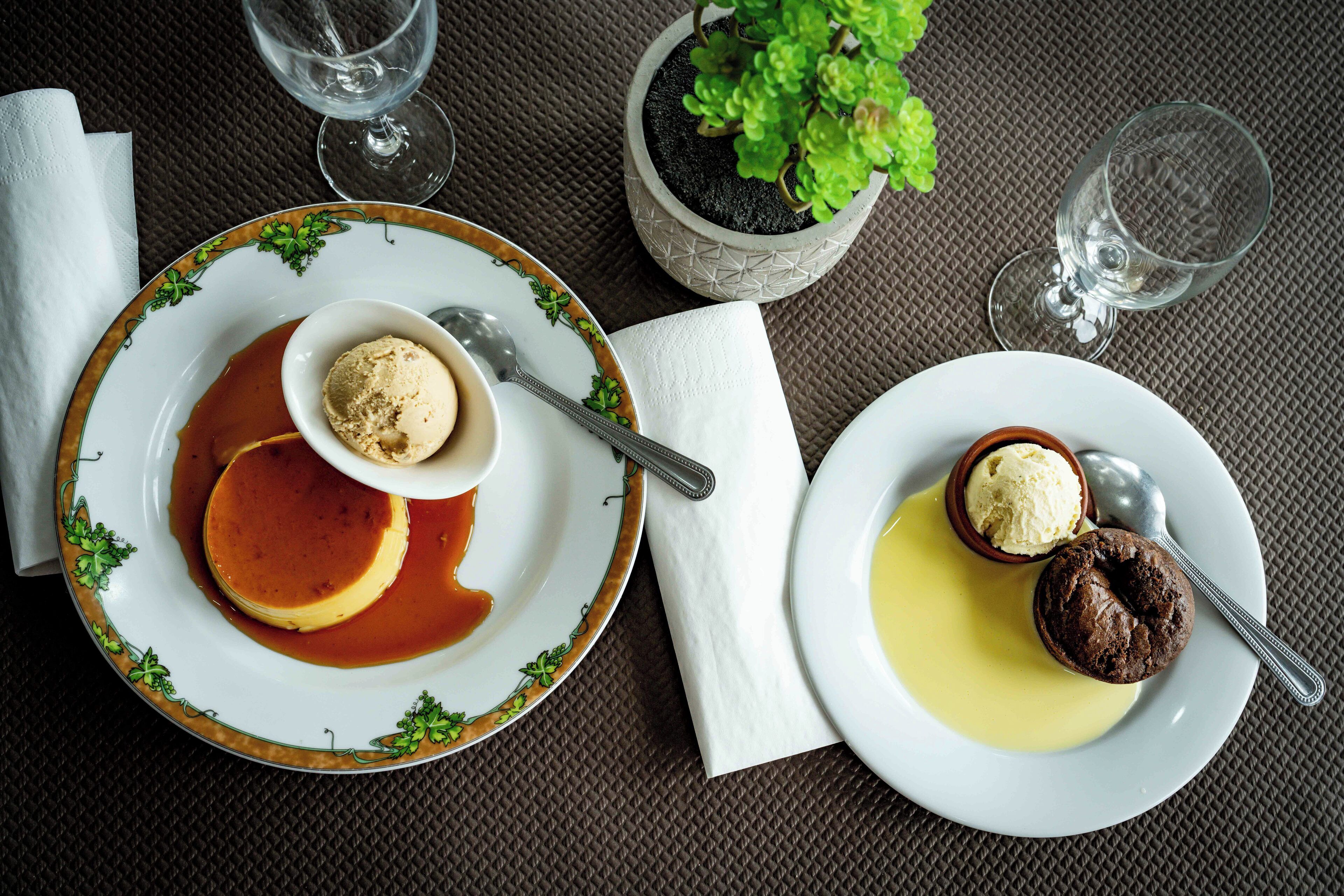 A dining table with plates of dessert, a potted plant, and empty wine glasses.