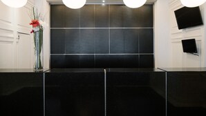 A reception area with a black marble counter, a large dark wall, and two mounted televisions.