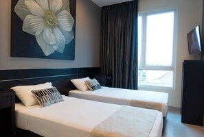Een hotelkamer met twee bedden, een groot bloemenkunstwerk, een televisie en een raam met gordijnen.