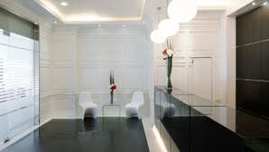 A modern reception area with a black marble counter, white chairs, and a vase with flowers.