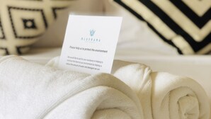 A neatly made bed with rolled white towels and a card asking for environmental protection. - Bluerama Resort (Ko Pha-ngan)