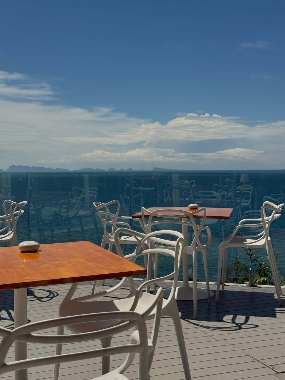 An outdoor seating area with white chairs and tables, overlooking a body of water and distant land.