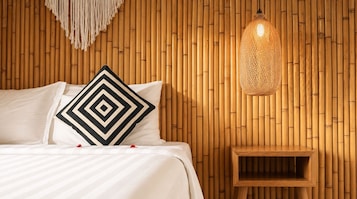 A bed with a geometric-patterned pillow, a hanging light fixture, and a wooden nightstand.