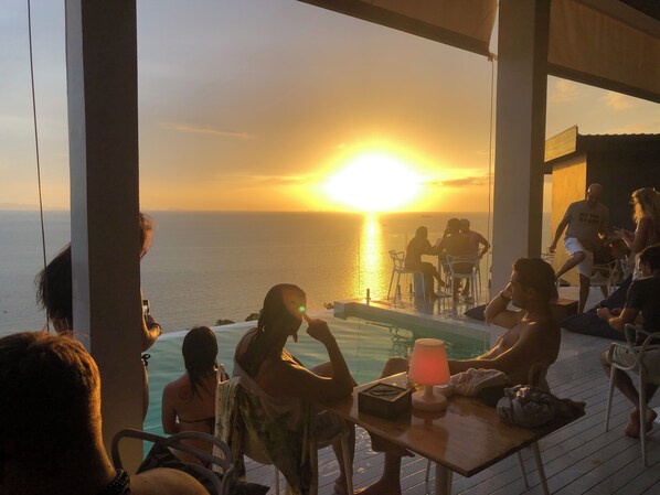 A sunset view from a poolside area with people seated at tables, overlooking the ocean. - Bluerama Resort (Ko Pha-ngan)
