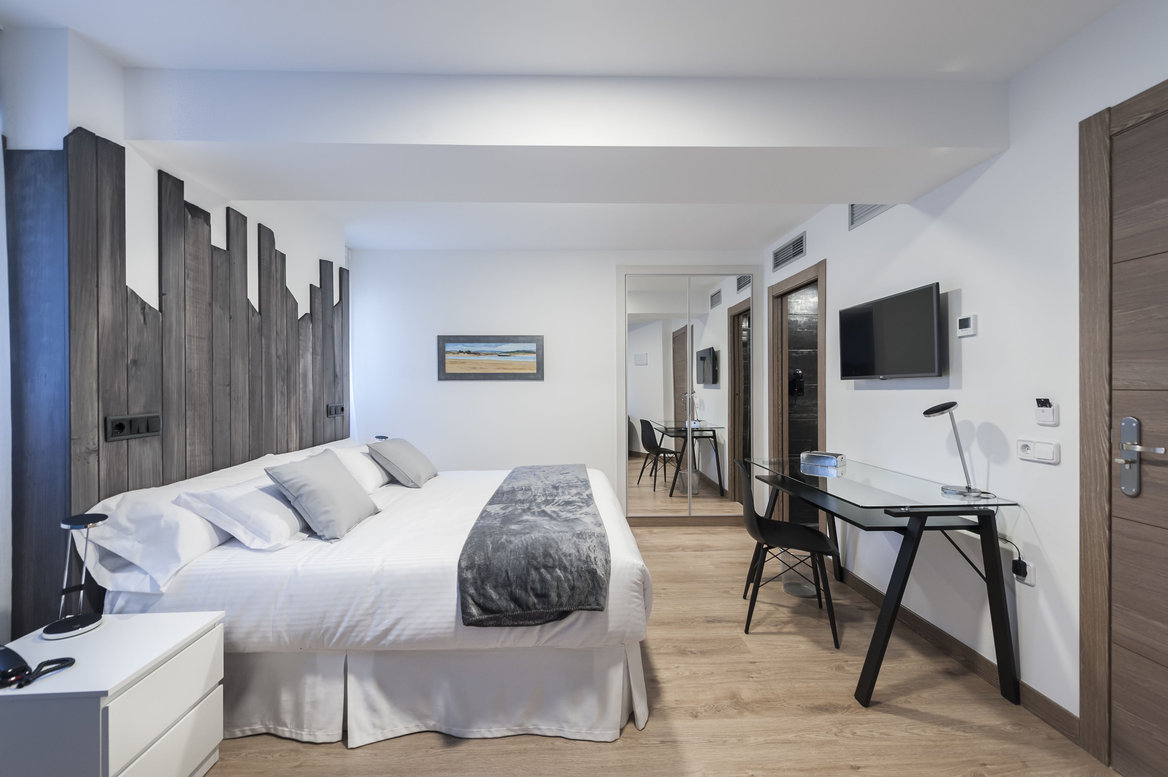 A modern hotel room with a bed, bedside table, desk, and a TV.