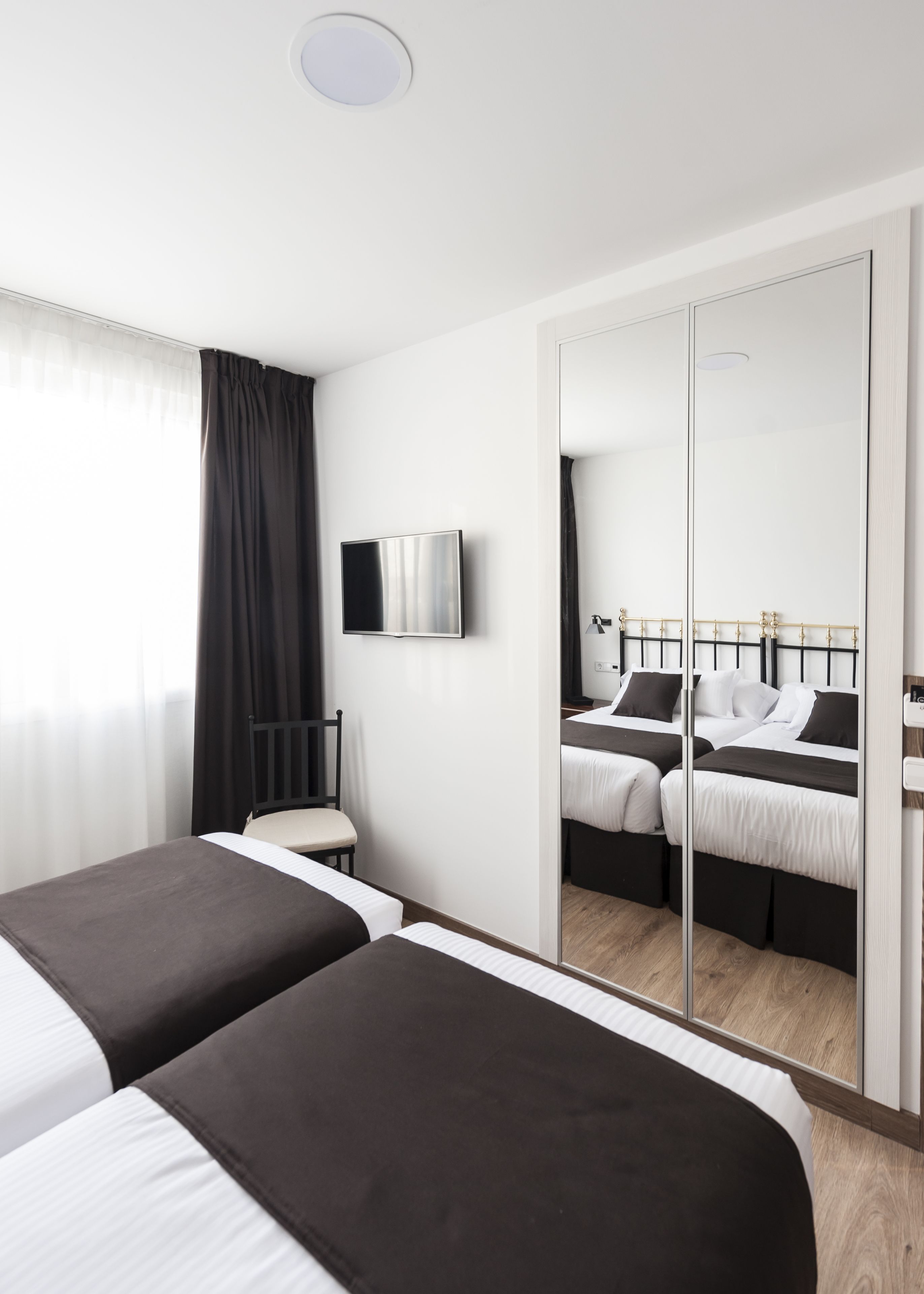 A modern hotel room with two beds, a large mirror, a flat-screen TV, and a wooden floor.