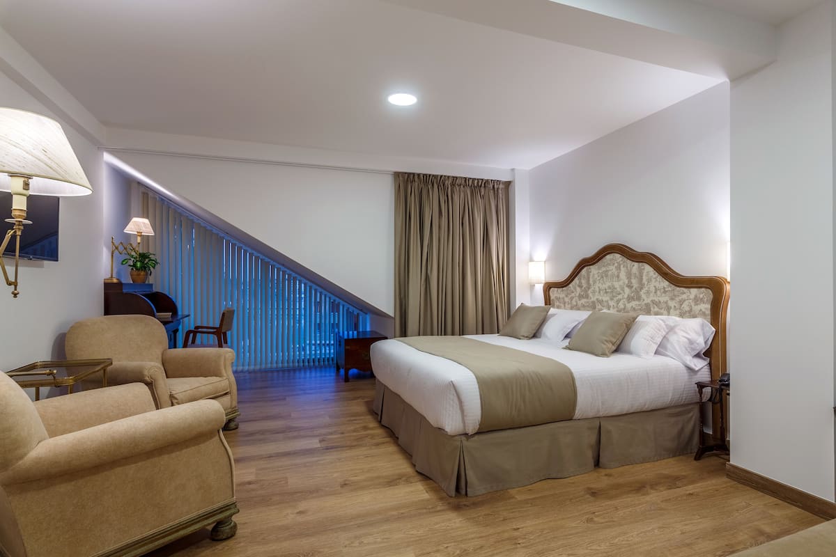 A hotel room with a bed, a chair, a desk, and a staircase.