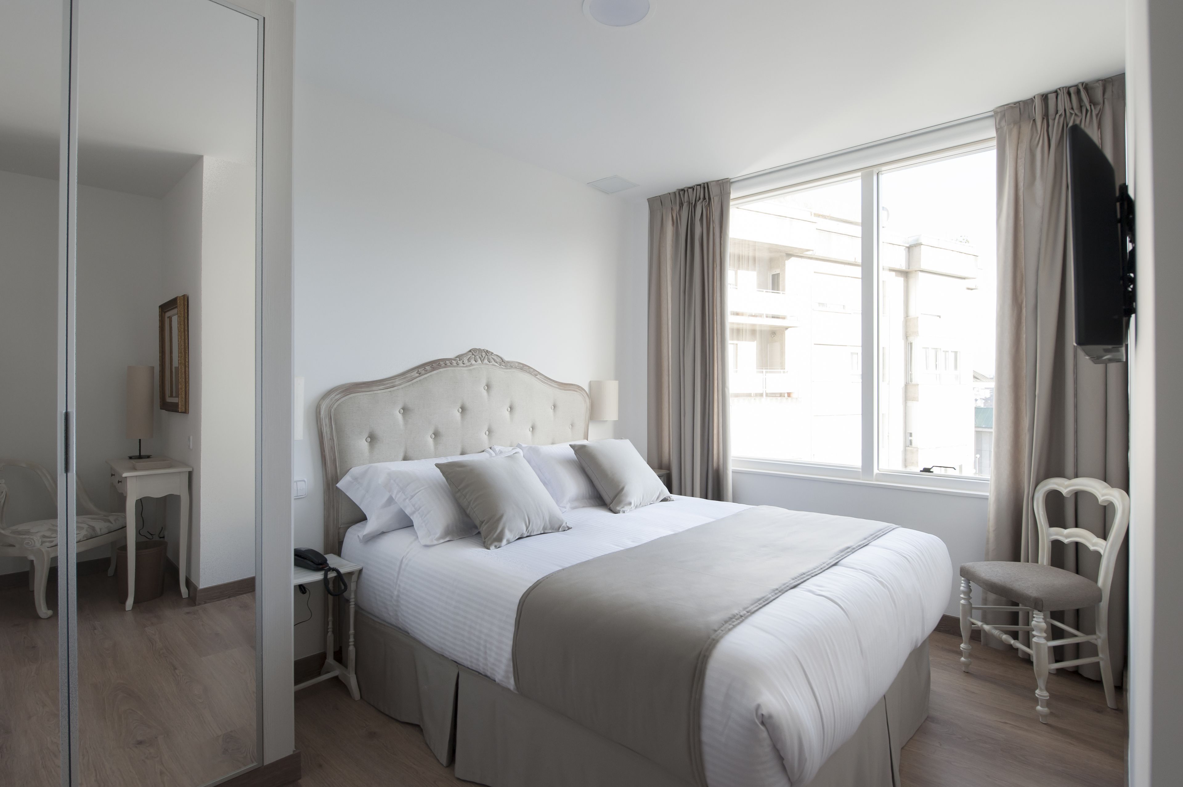 A neatly arranged bedroom with a large bed, a bedside table, a chair, and a television mounted on the wall.