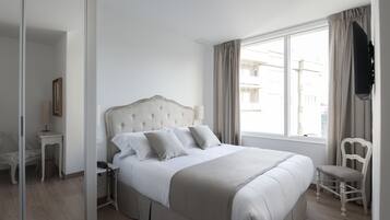 A neatly arranged bedroom with a large bed, a bedside table, a chair, and a television mounted on the wall.