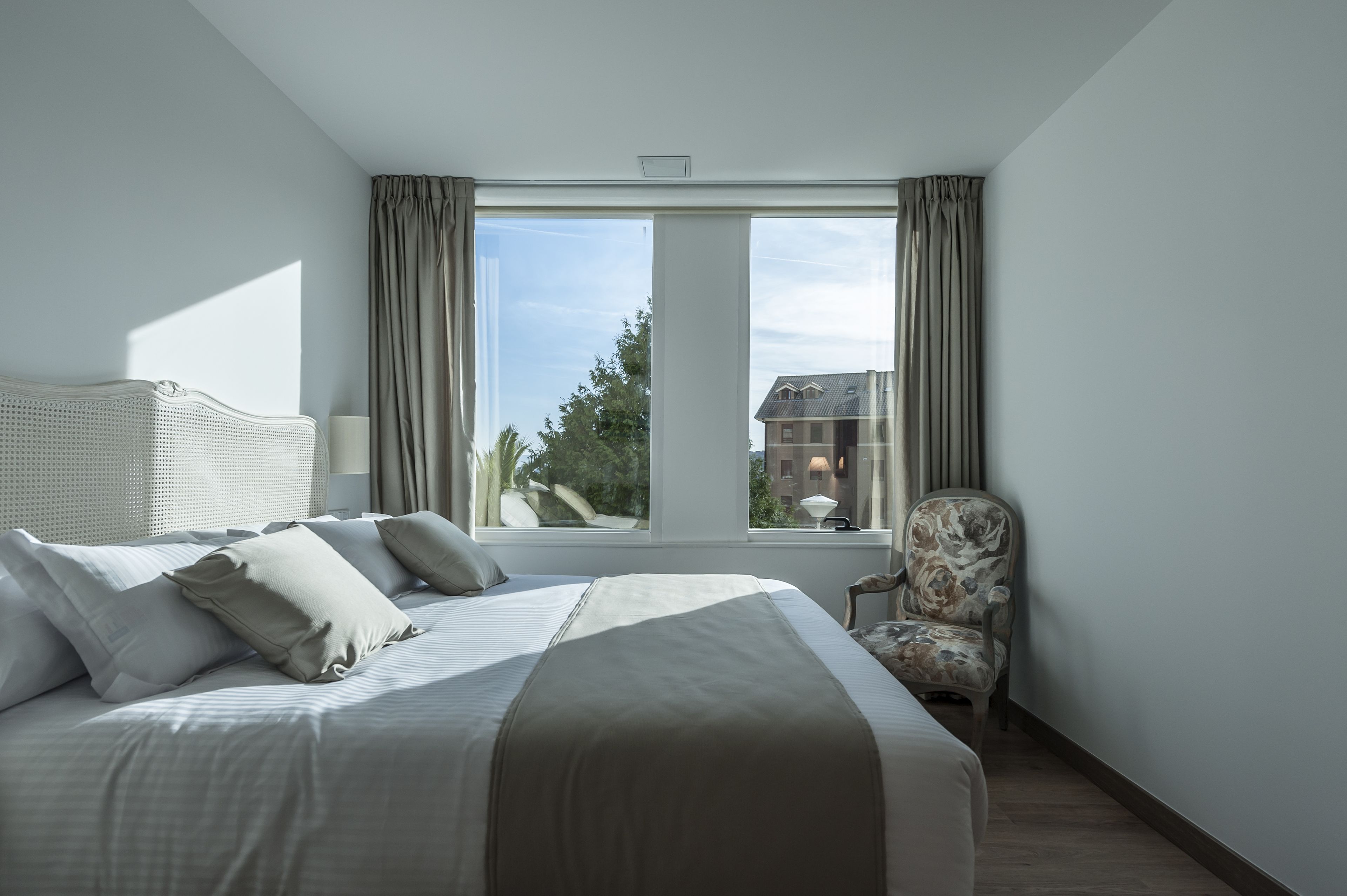 Een hotelkamer met een groot bed, een stoel en een raam met gordijnen.