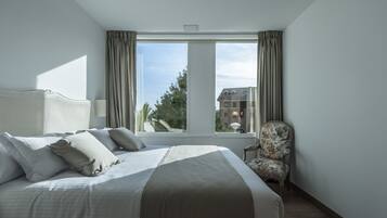 Een hotelkamer met een groot bed, een stoel en een raam met gordijnen.