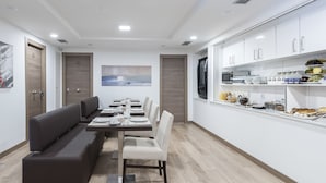 Een moderne eethoek met een lange tafel, banken en een keukentafel met etenswaren.