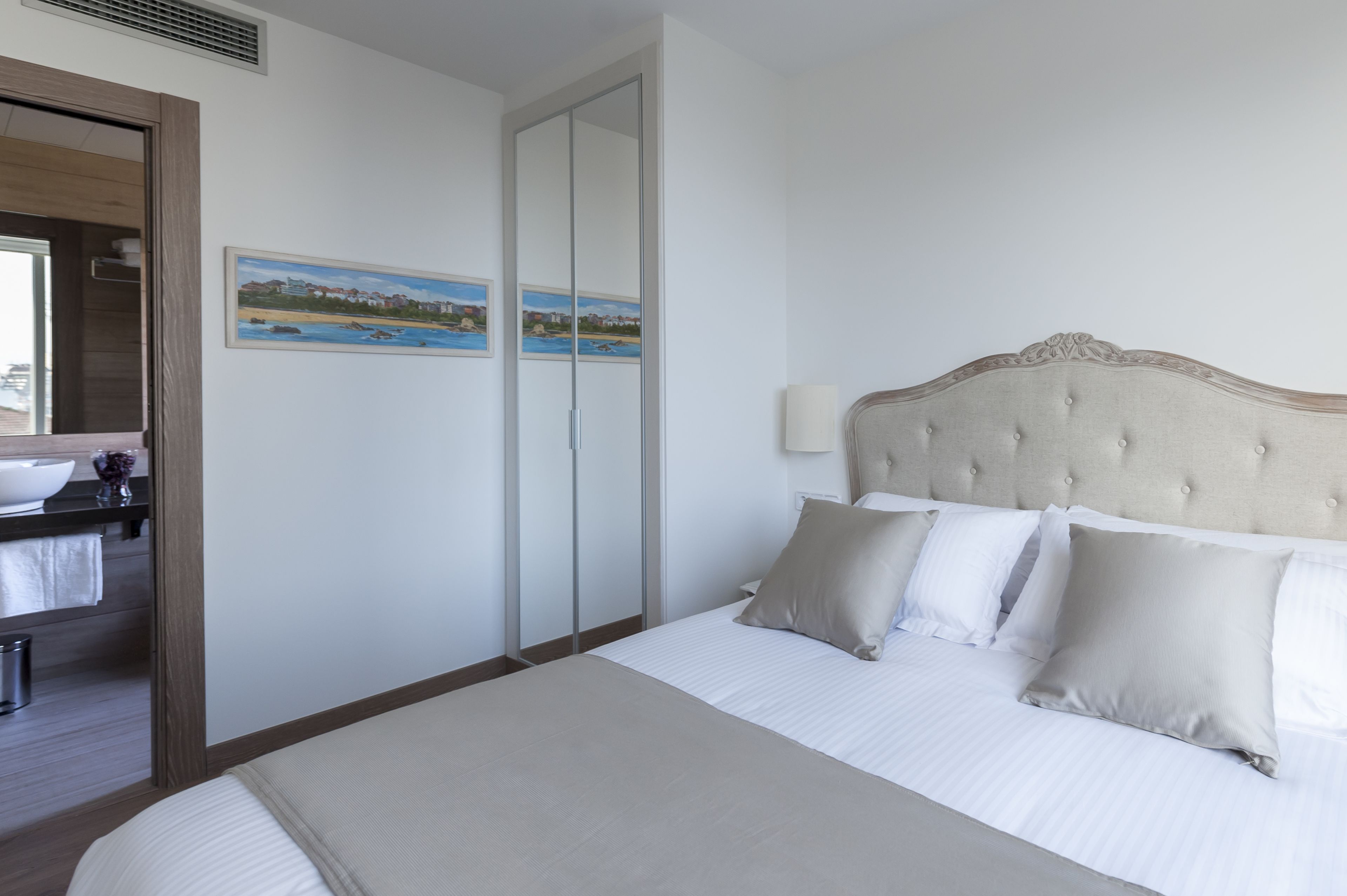 Una habitación de hotel con cama, mesita de noche, espejo y un cuadro en la pared.