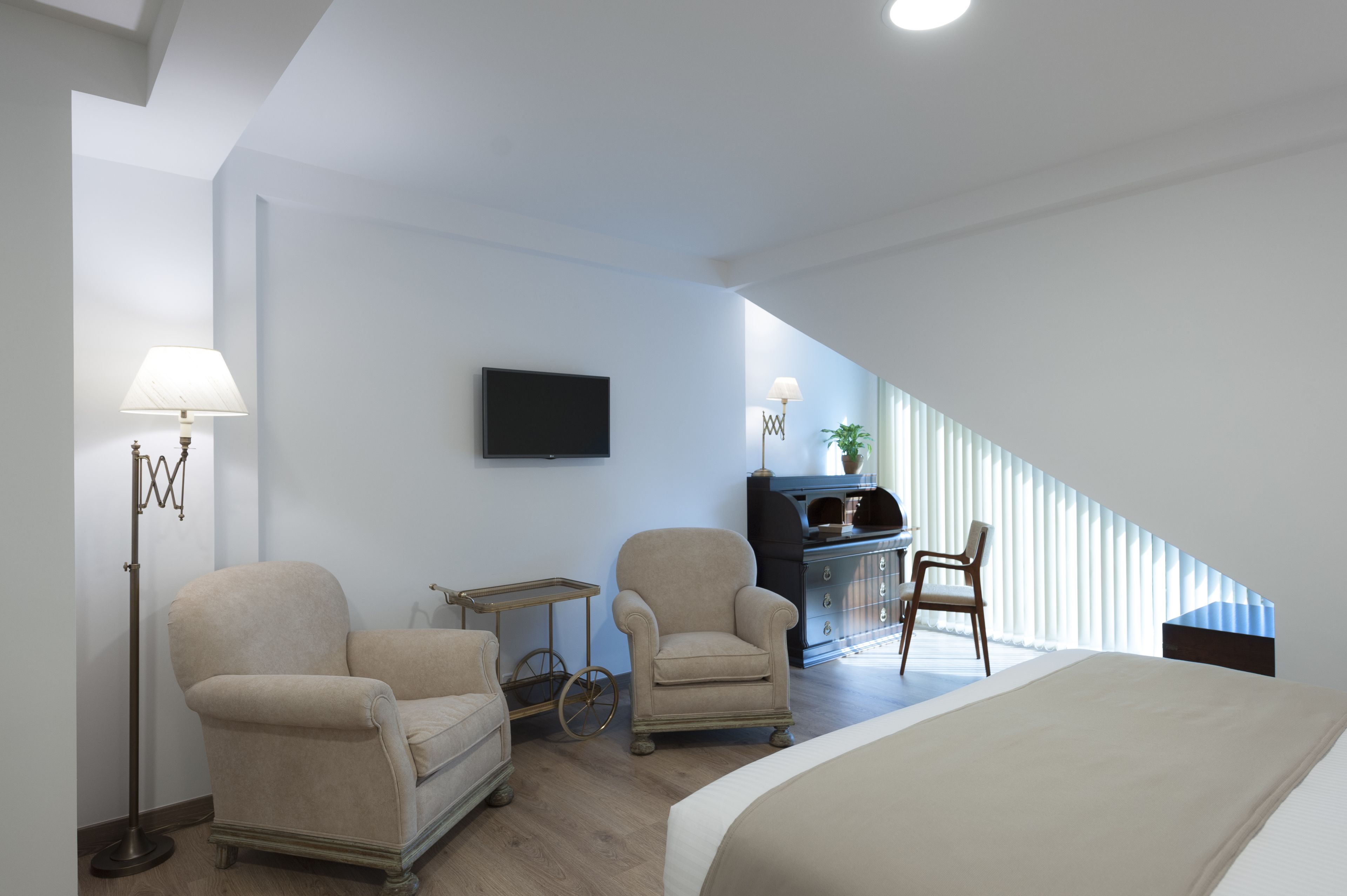 A modern hotel room with a large bed, two armchairs, a desk, and a television.
