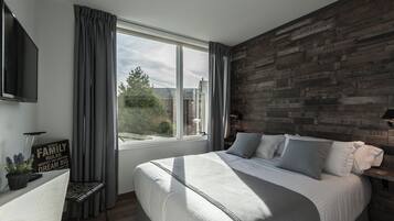Un dormitorio con una cama grande, un televisor montado en la pared, una ventana con cortinas y una pared de acento de madera.