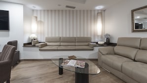 Een moderne woonkamer met een beige bank, een glazen salontafel en een gestreepte wand.
