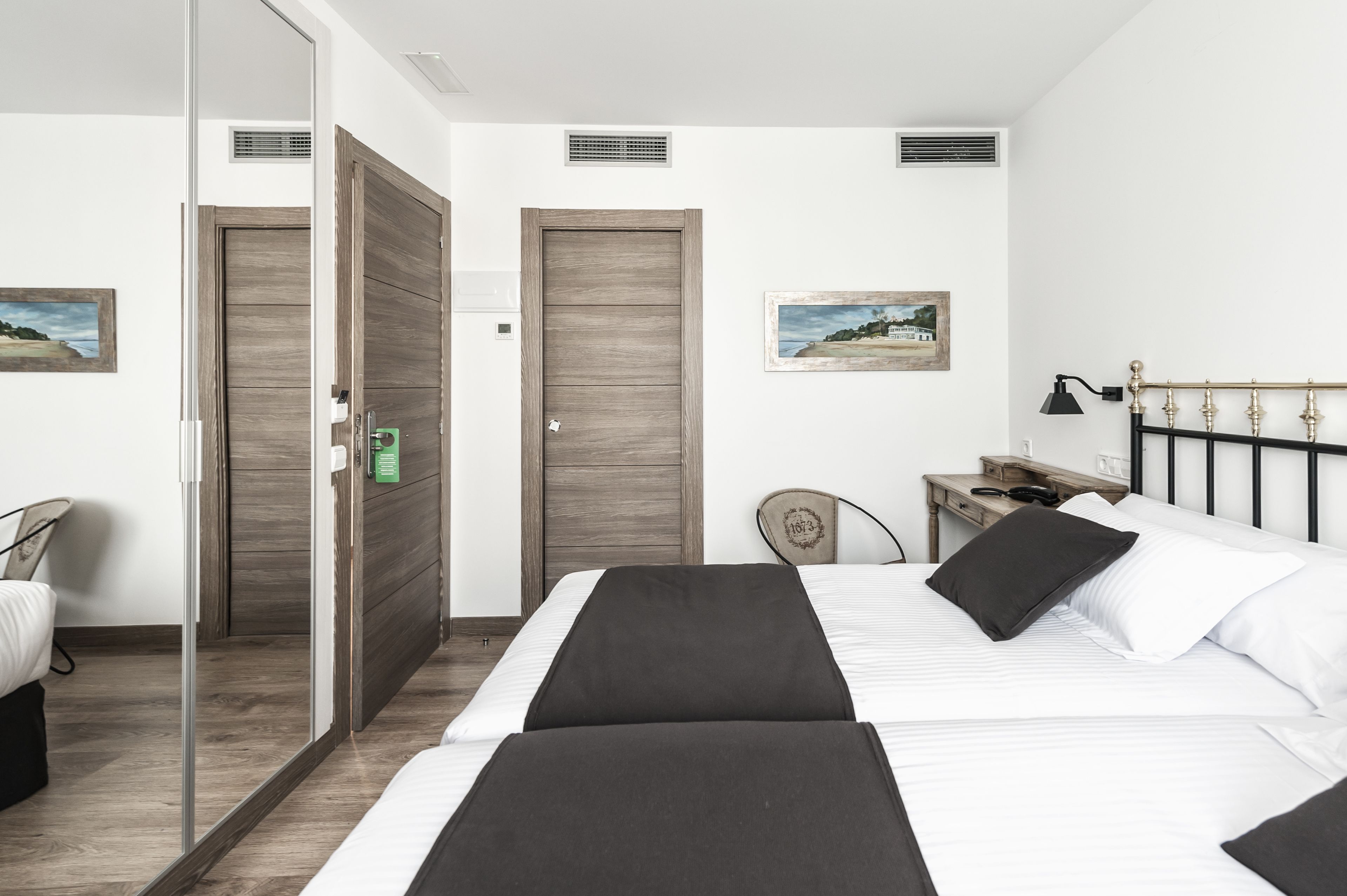 A hotel room with a bed, a desk, a chair, and two doors.