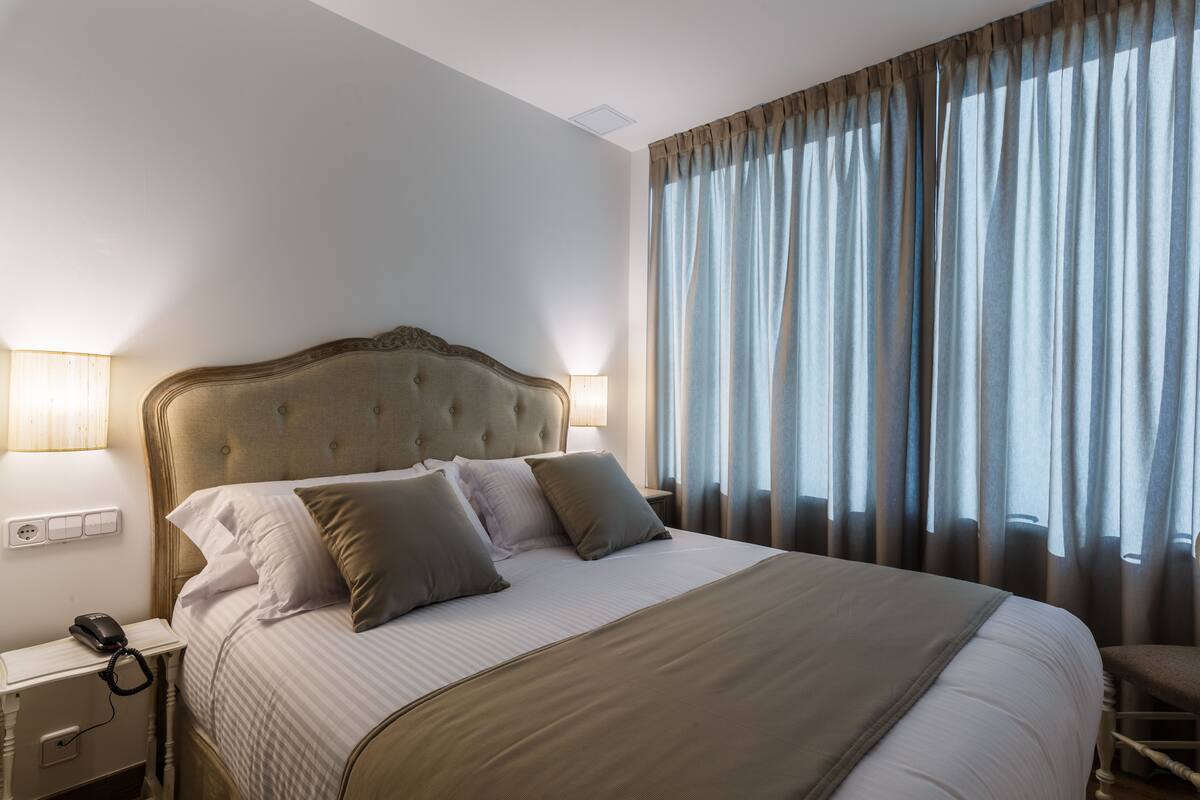 A neatly made bed with a tufted headboard, a bedside lamp, and a power outlet on the nightstand.