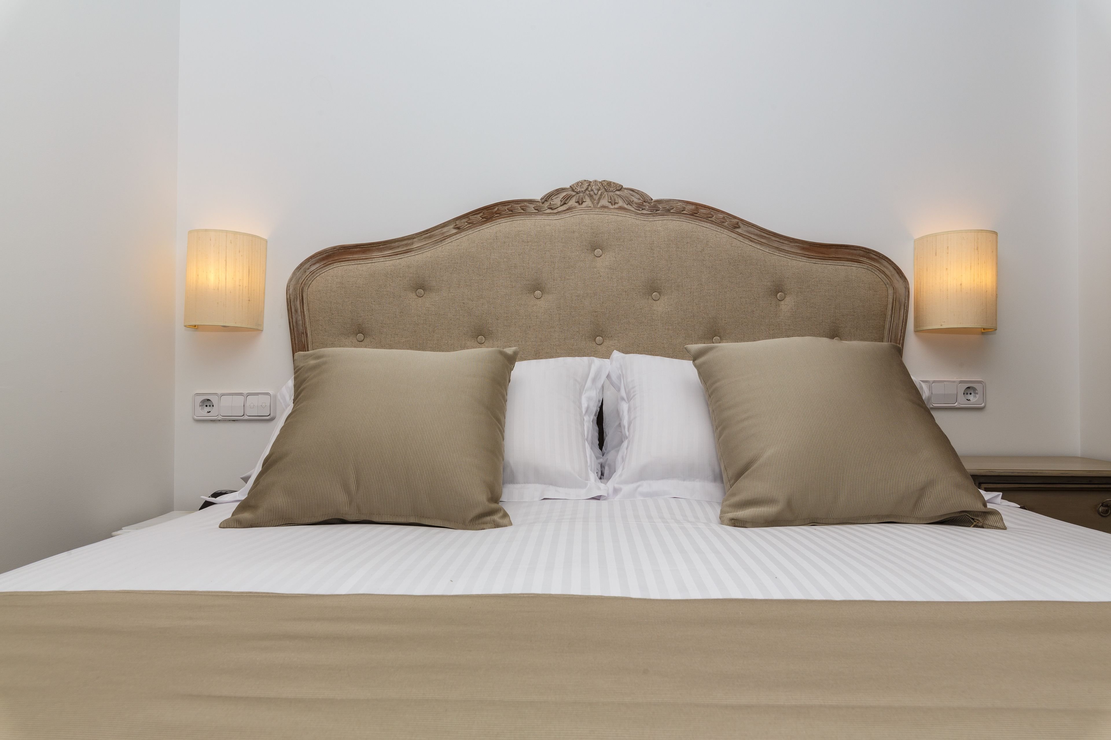 A neatly made bed with a tufted headboard, two beige pillows, and a white duvet.
