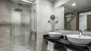 Un baño moderno con ducha de vidrio, dos lavamanos y un espejo grande.