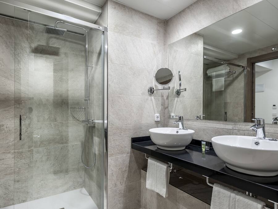 Un baño moderno con ducha de vidrio, dos lavamanos y un espejo grande.