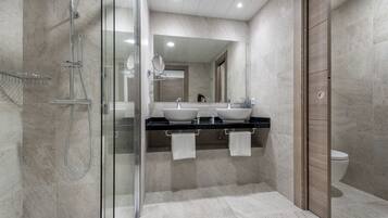 Un baño moderno con cabina de ducha de vidrio, dos lavamanos y un espejo grande.