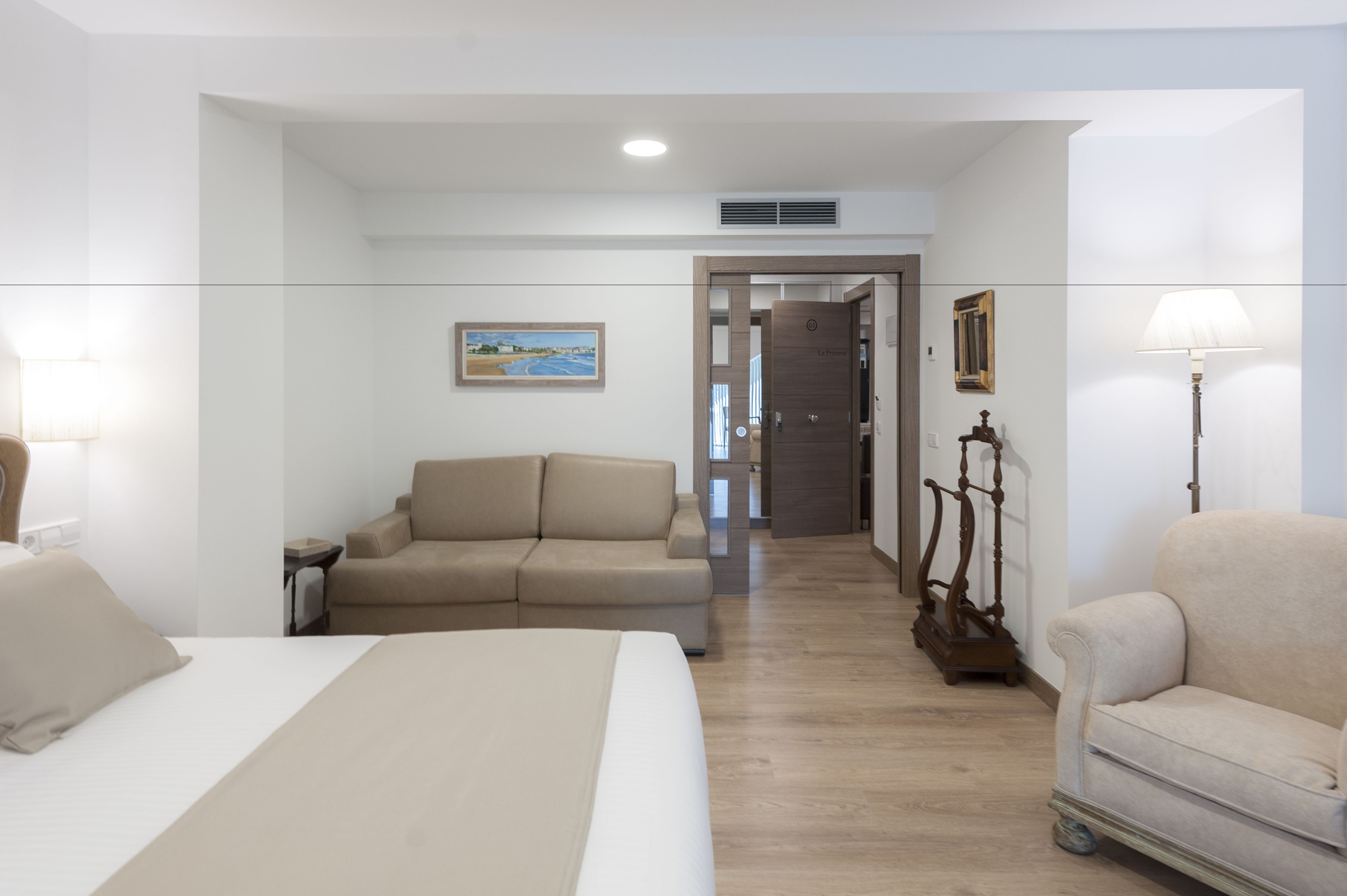 A hotel room with a bed, two sofas, a lamp, and a painting on the wall.