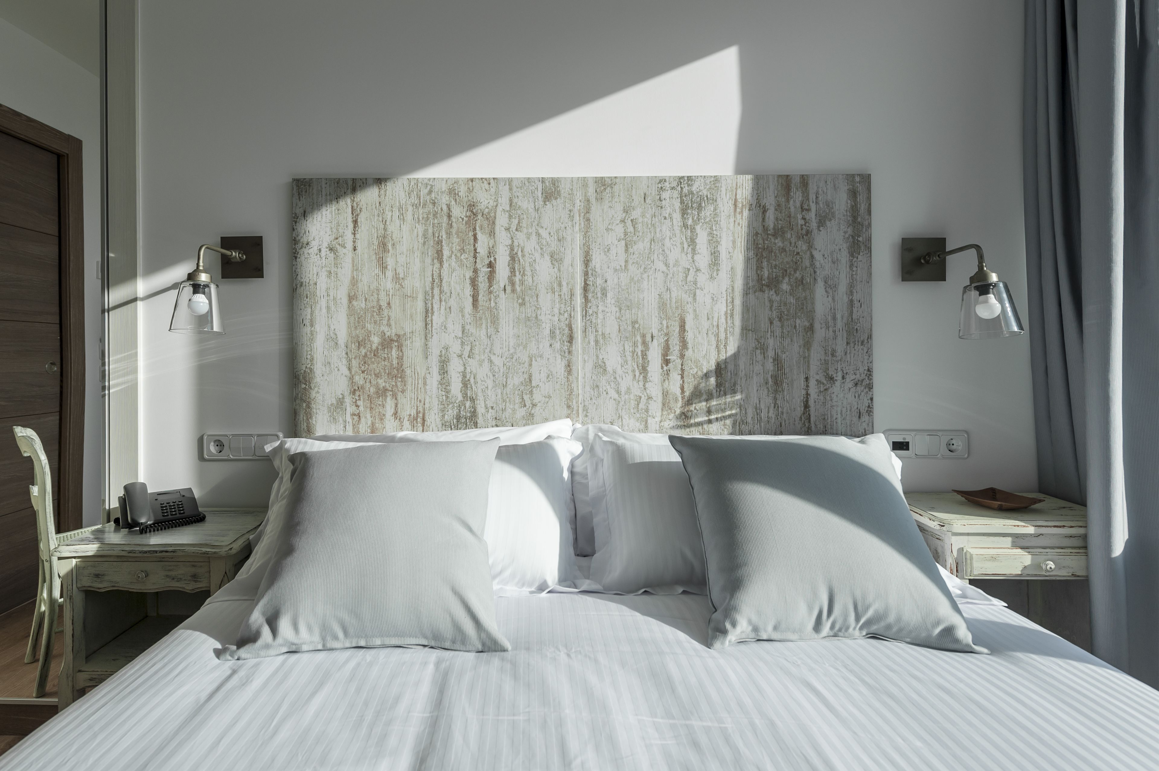 A neatly made bed with white linens, a wooden headboard, bedside tables with lamps, and a telephone.