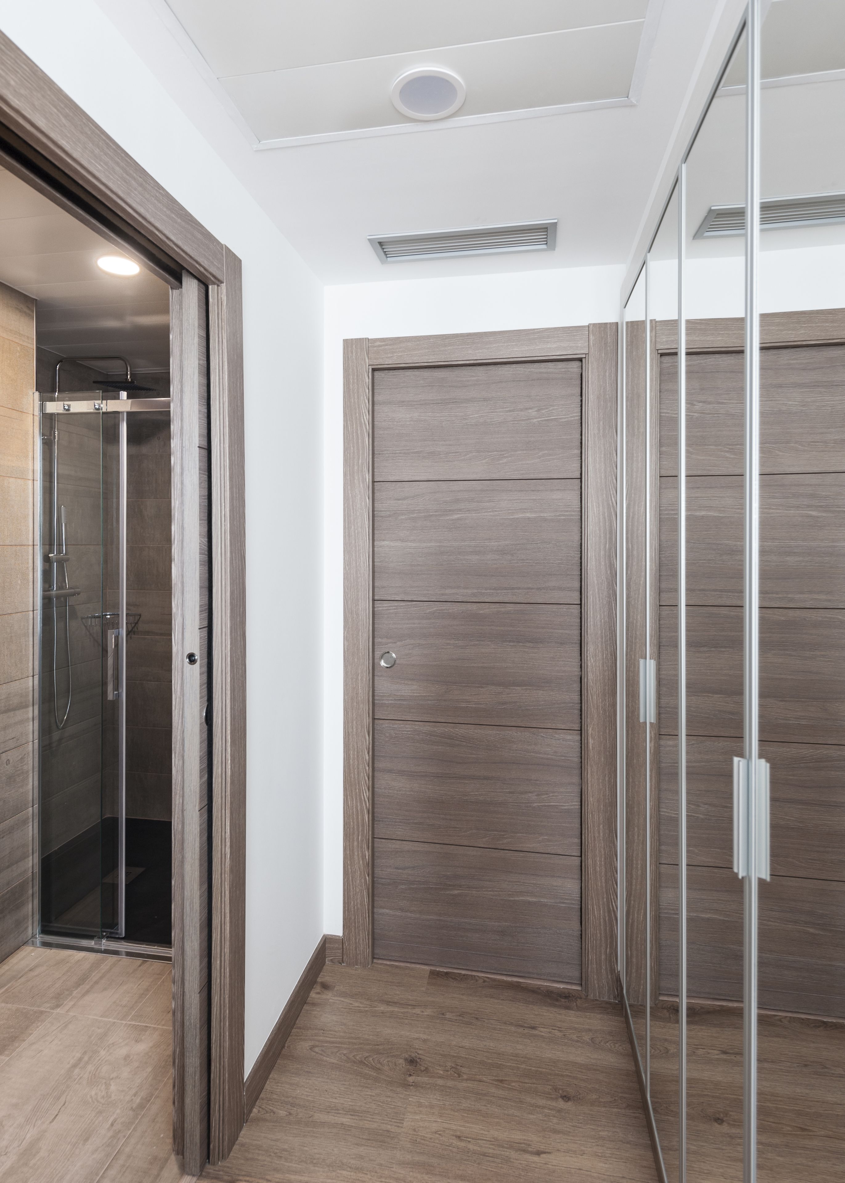 Un baño moderno con cabina de ducha de vidrio, suelo de madera y un amplio armario con puerta de espejo.