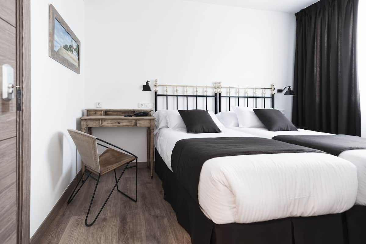 A hotel room with a bed, a desk, a chair, and a picture on the wall.