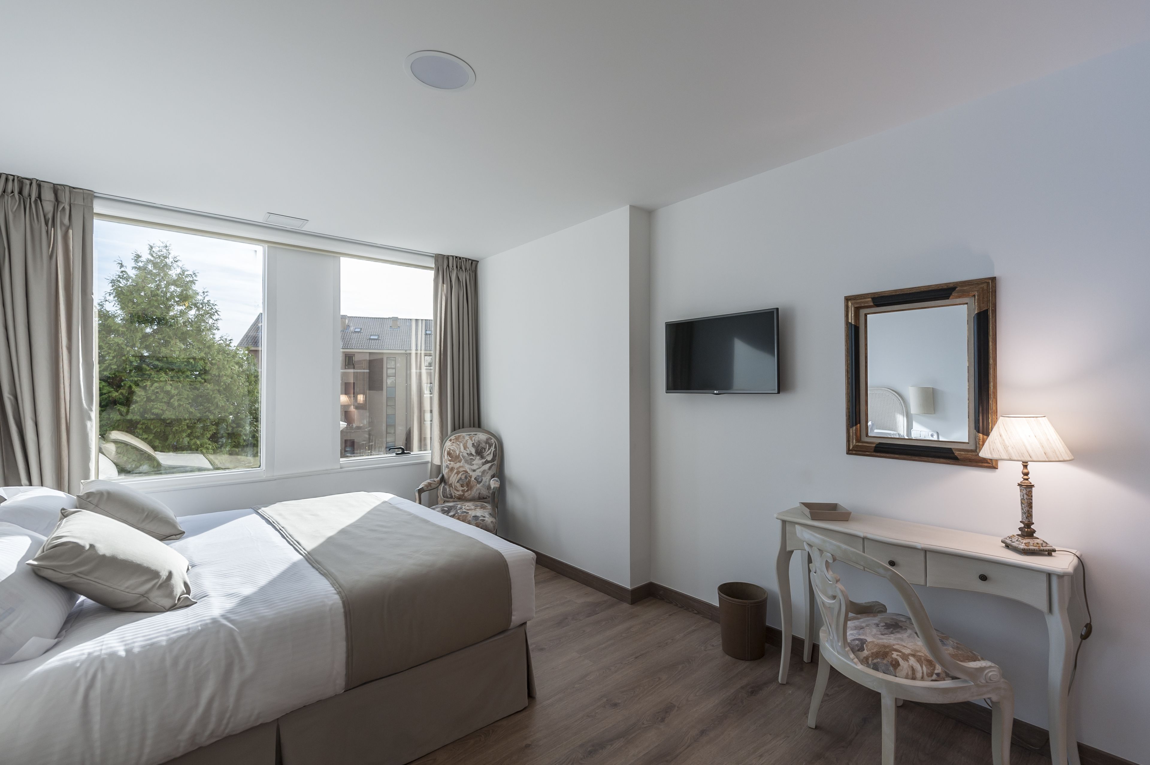 Una habitación de hotel con cama, escritorio, silla, televisor y ventana con cortinas.