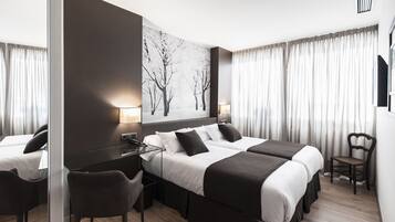 Habitación de hotel con dos camas, un escritorio, una silla, un ventanal con cortinas y un televisor de pared.
