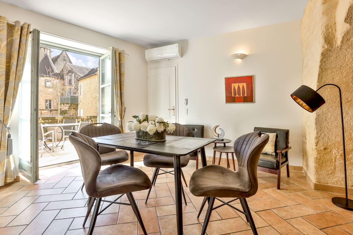 Un coin repas avec une table et des chaises, une cheminée et une vue sur un bâtiment par une porte ouverte.