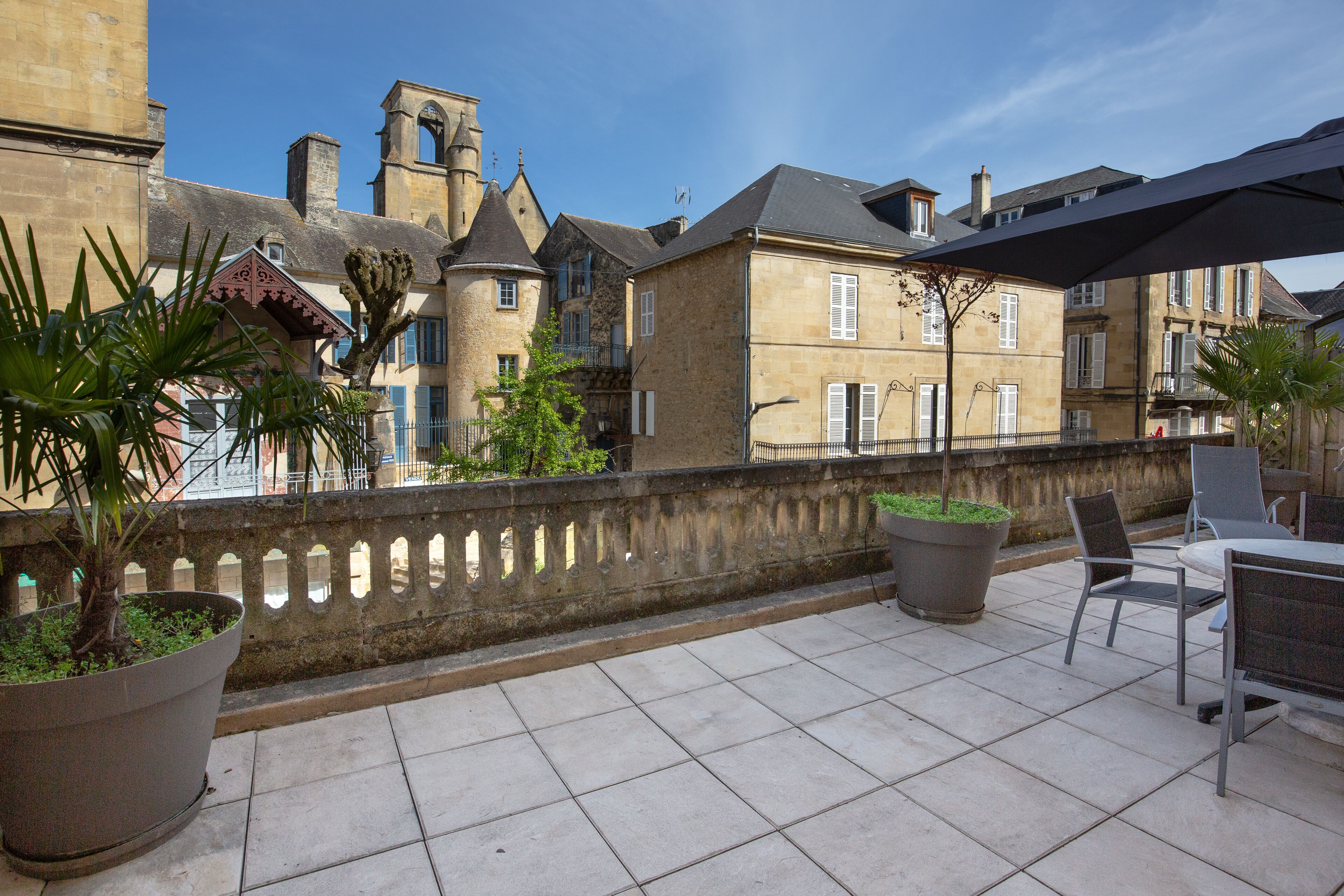 A terrace with outdoor seating, a stone balustrade, and historic buildings in the background.