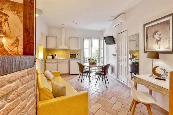 Una cocina moderna con armarios blancos, una zona de comedor con mesa y sillas, y una sala de estar con un sofá amarillo.
