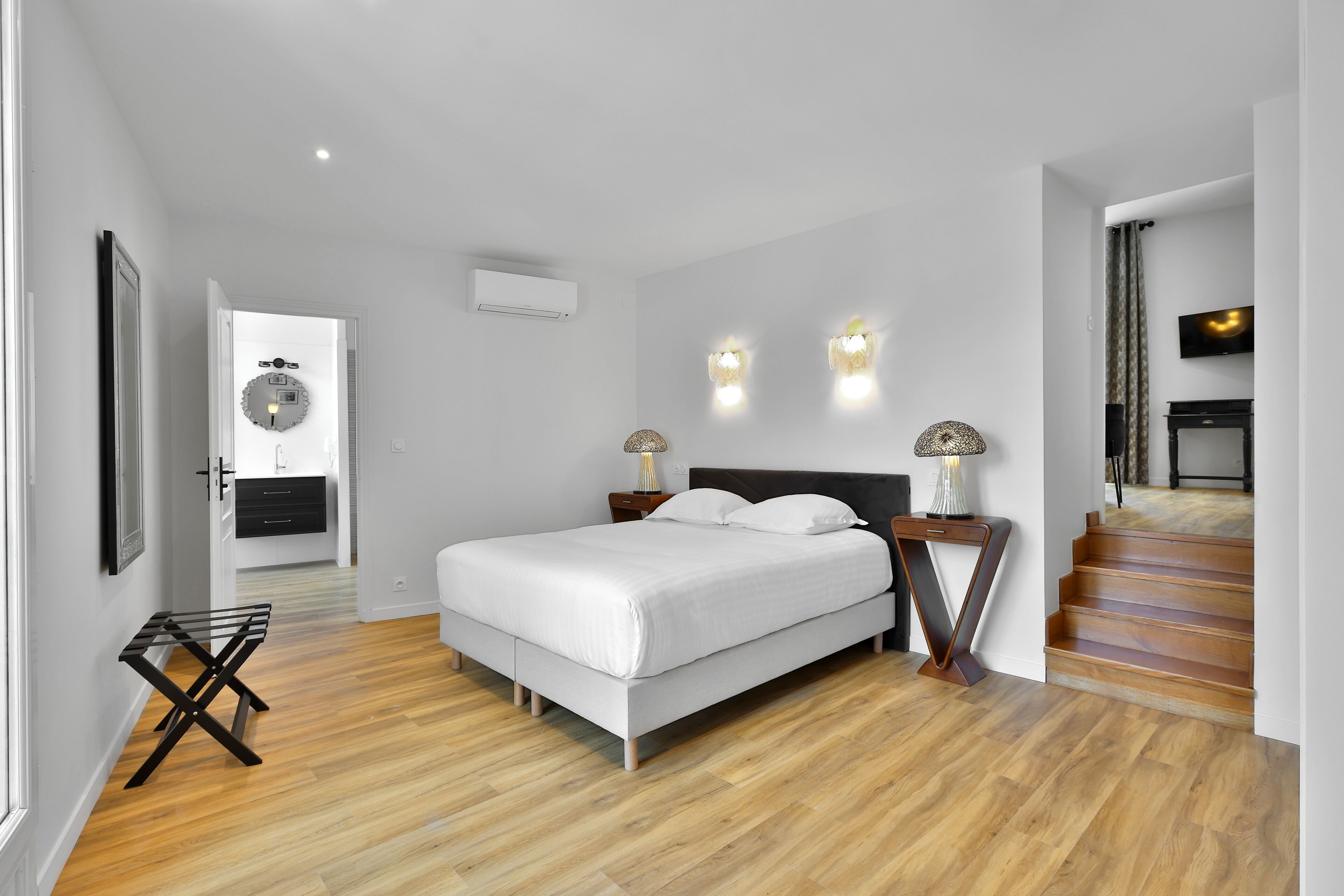 Une chambre moderne avec un grand lit, un plancher en bois, une armoire intégrée et un escalier menant à un niveau supérieur.