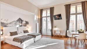 Quarto de hotel moderno com uma cama grande, duas mesas de cabeceira, uma TV de tela plana e um espaço de refeições com mesa e cadeiras.