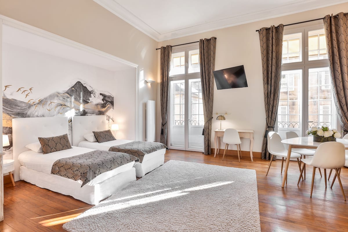 Une chambre d’hôtel moderne dotée d’un grand lit, de deux tables de chevet, d’un téléviseur à écran plat et d’un coin repas avec une table et des chaises.