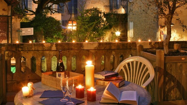 Uma área de refeições ao ar livre com uma mesa posta para dois, rodeada de cadeiras e um ambiente acolhedor à luz de velas.
