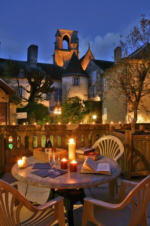 Un área de comedor al aire libre con una mesa para dos, rodeada de sillas y un ambiente cálido a la luz de las velas.