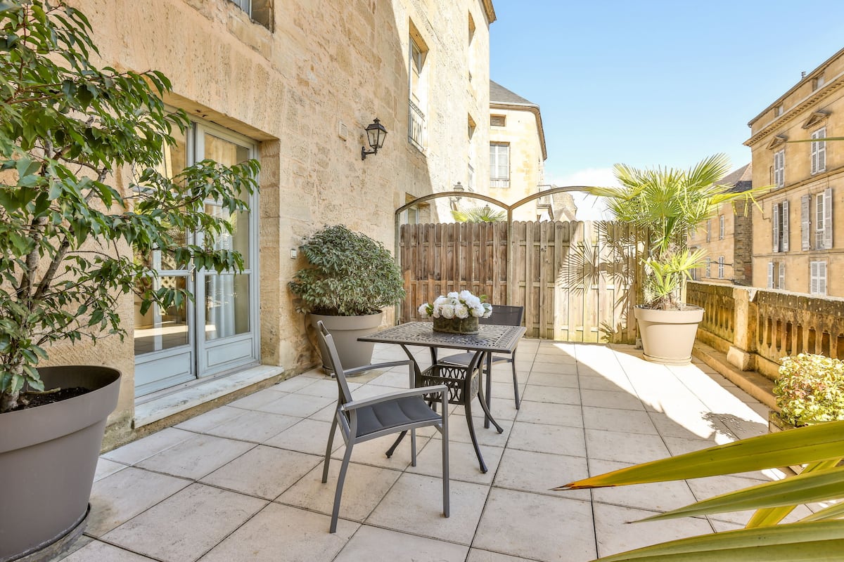 Une terrasse avec une table et des chaises, des plantes en pot et une clôture en bois.