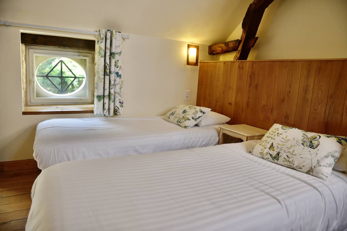 Une chambre avec deux lits, une fenêtre donnant sur un beau paysage, des boiseries et une table de chevet.