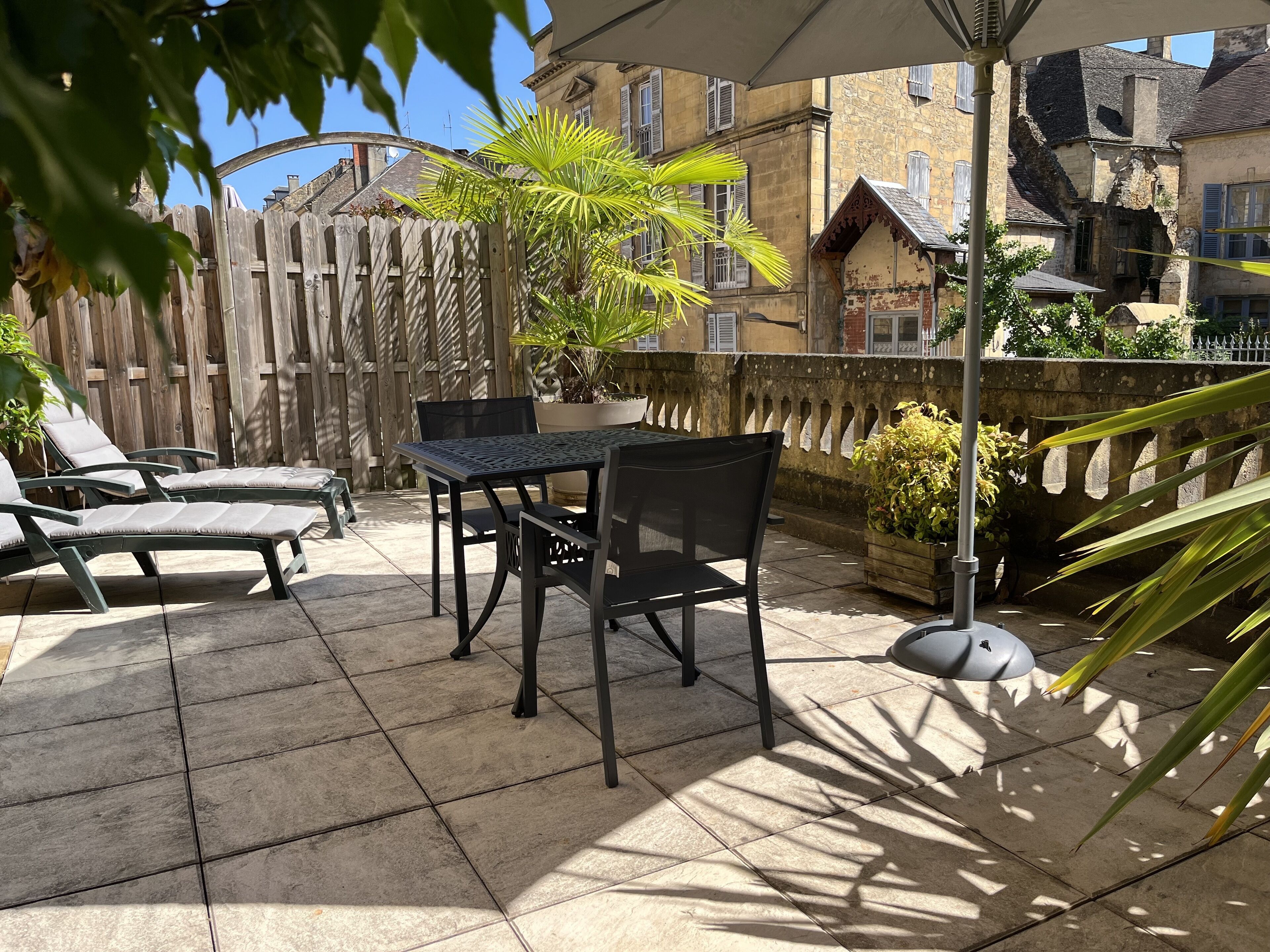 A patio with a table and chairs, a wooden fence, and potted plants.