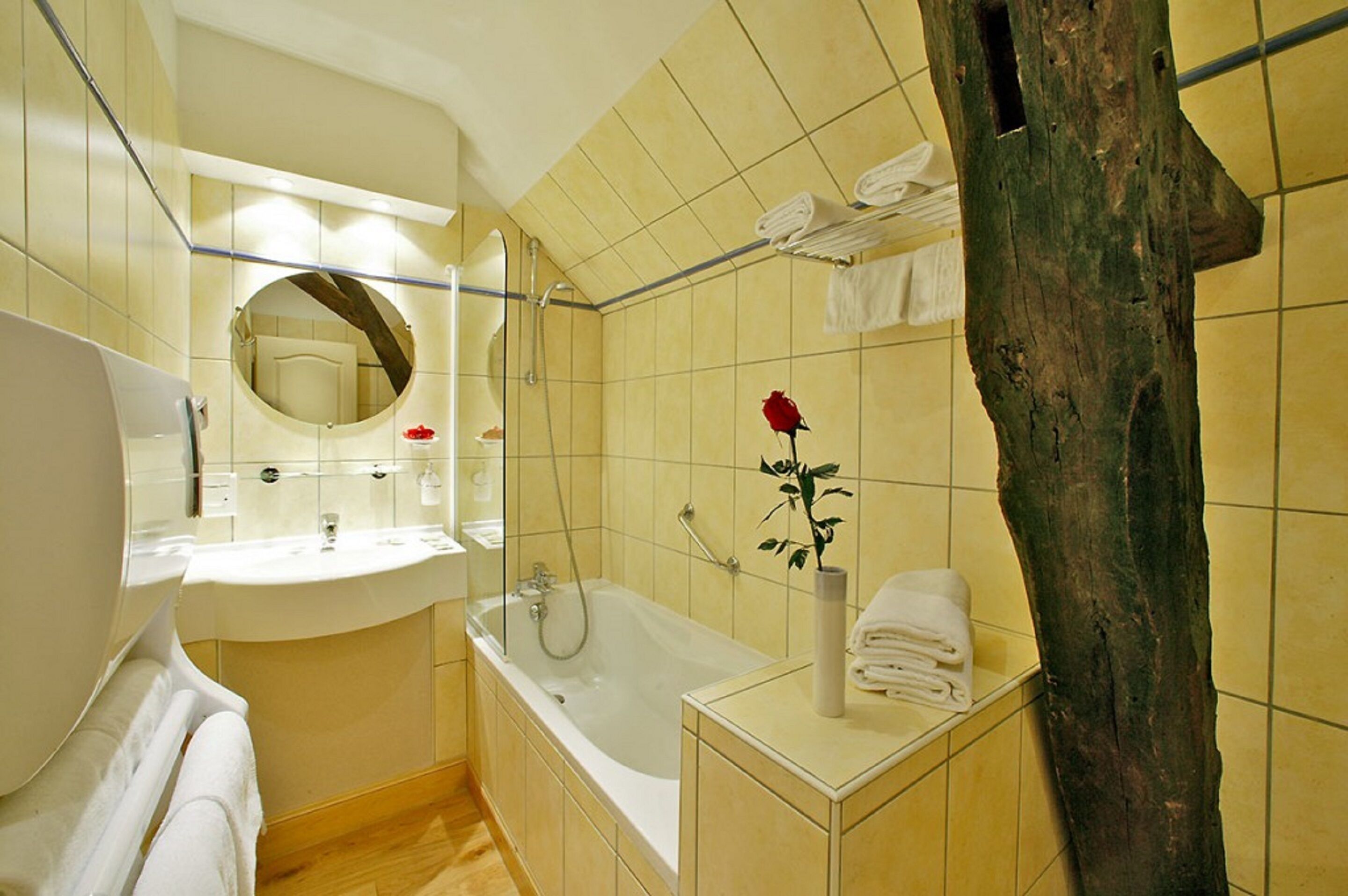 A modern bathroom with a bathtub, a round mirror, and a wooden tree trunk.