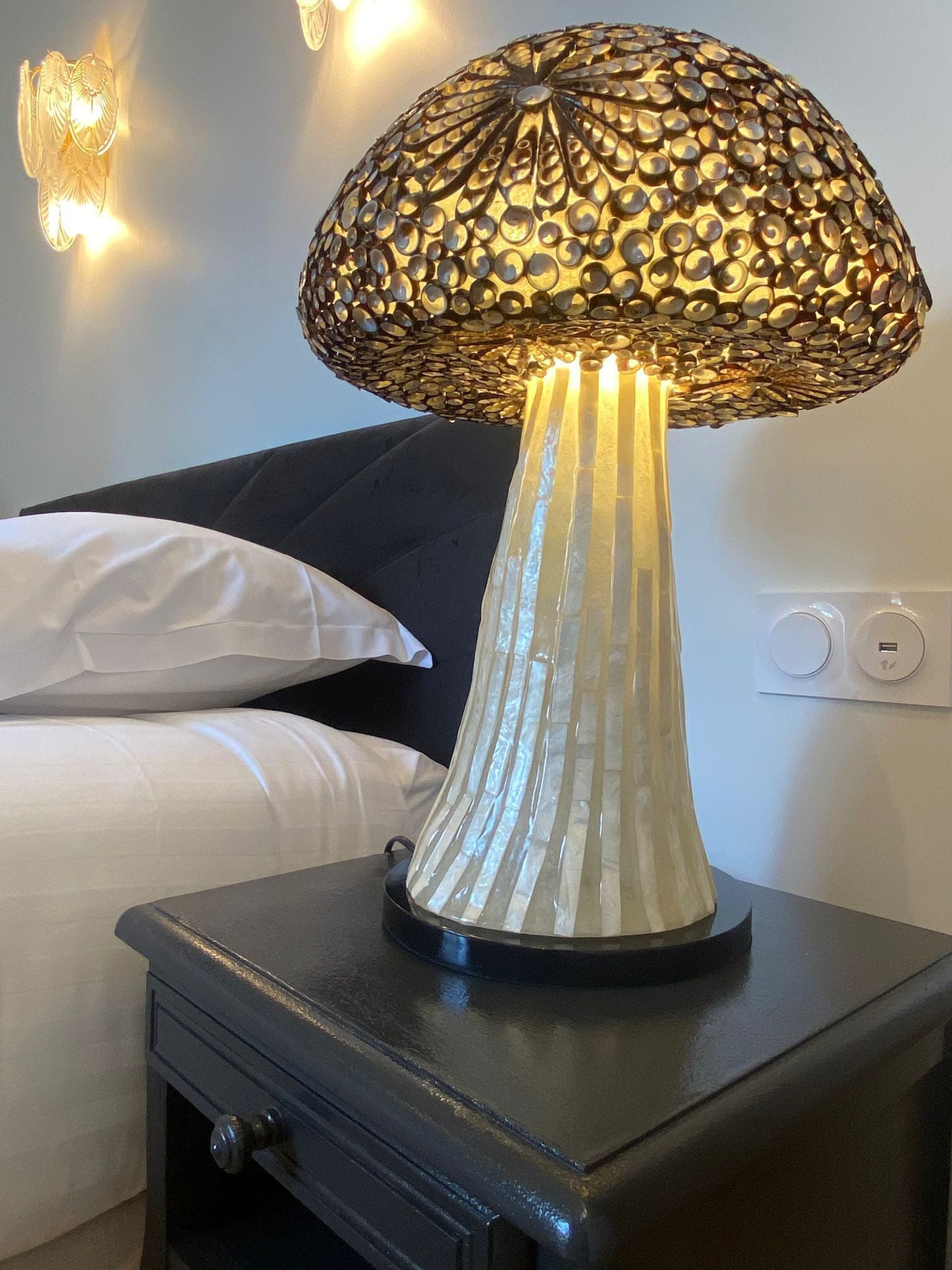 Eine Lampe mit einem strukturierten, gemusterten Lampenschirm auf einem Nachttisch in einem Hotelzimmer.