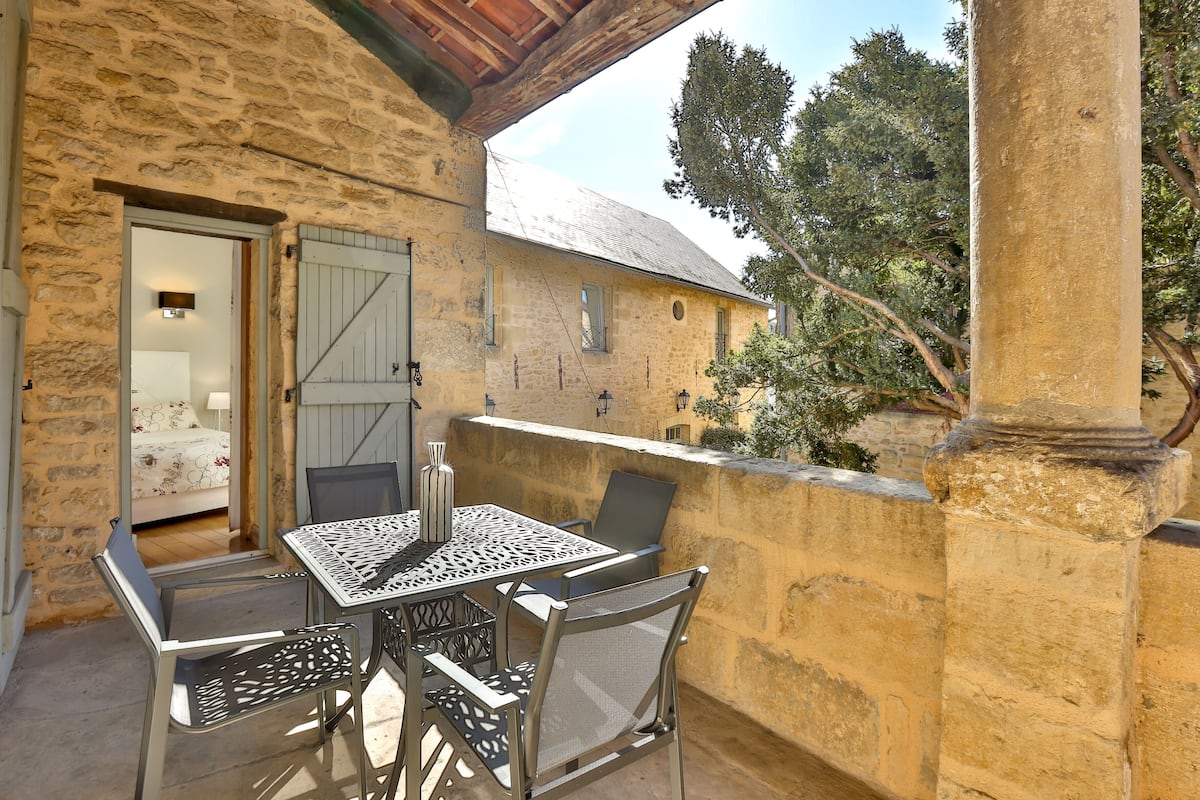 Un bâtiment en pierre doté d’un balcon où se trouvent une table et des chaises.