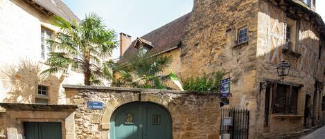 A historic stone building with a green door, a sign reading "Rue L. Roux," and a cobblestone street.