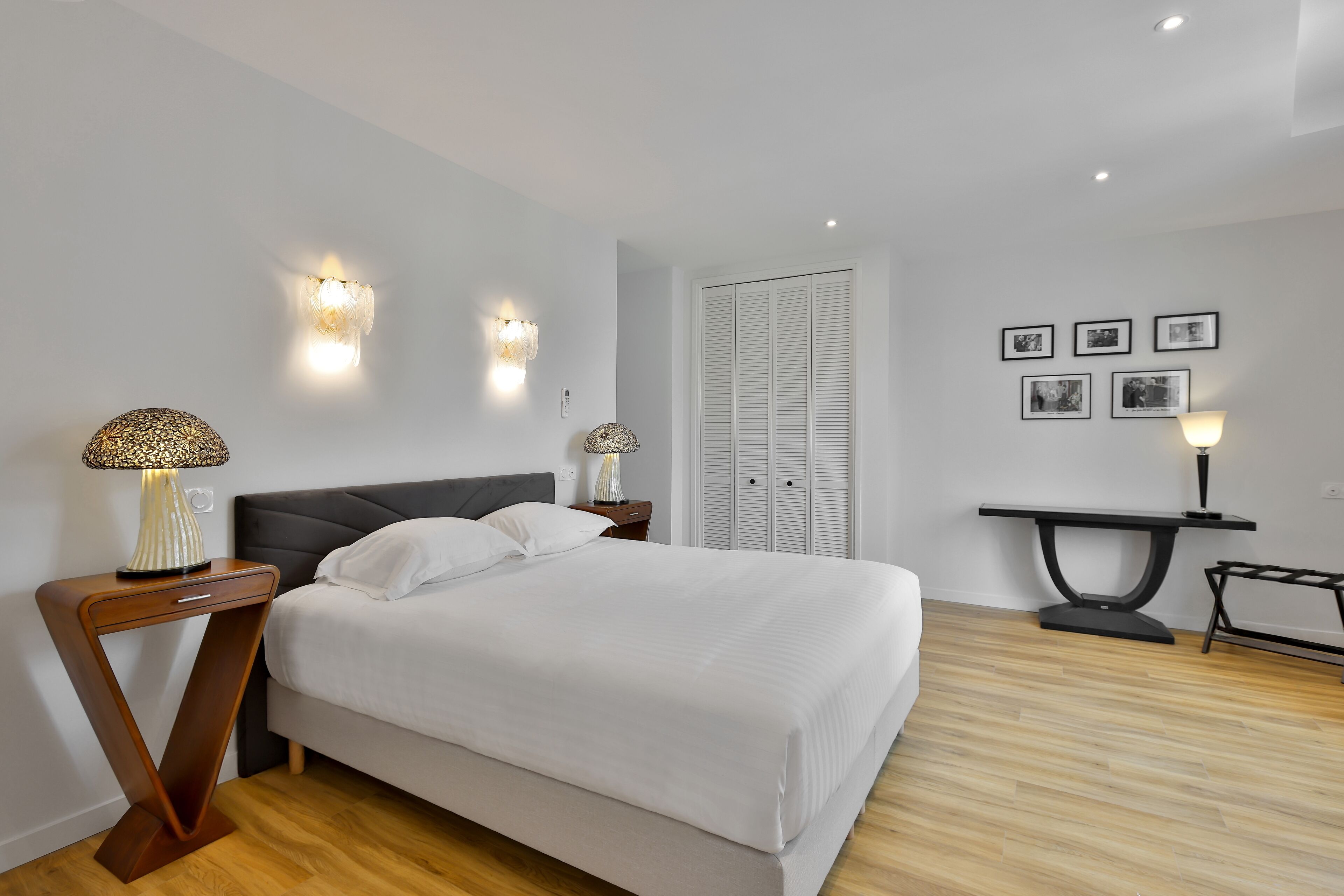 A modern bedroom with a bed, bedside tables, wall-mounted lights, a wardrobe, and framed pictures on the wall.