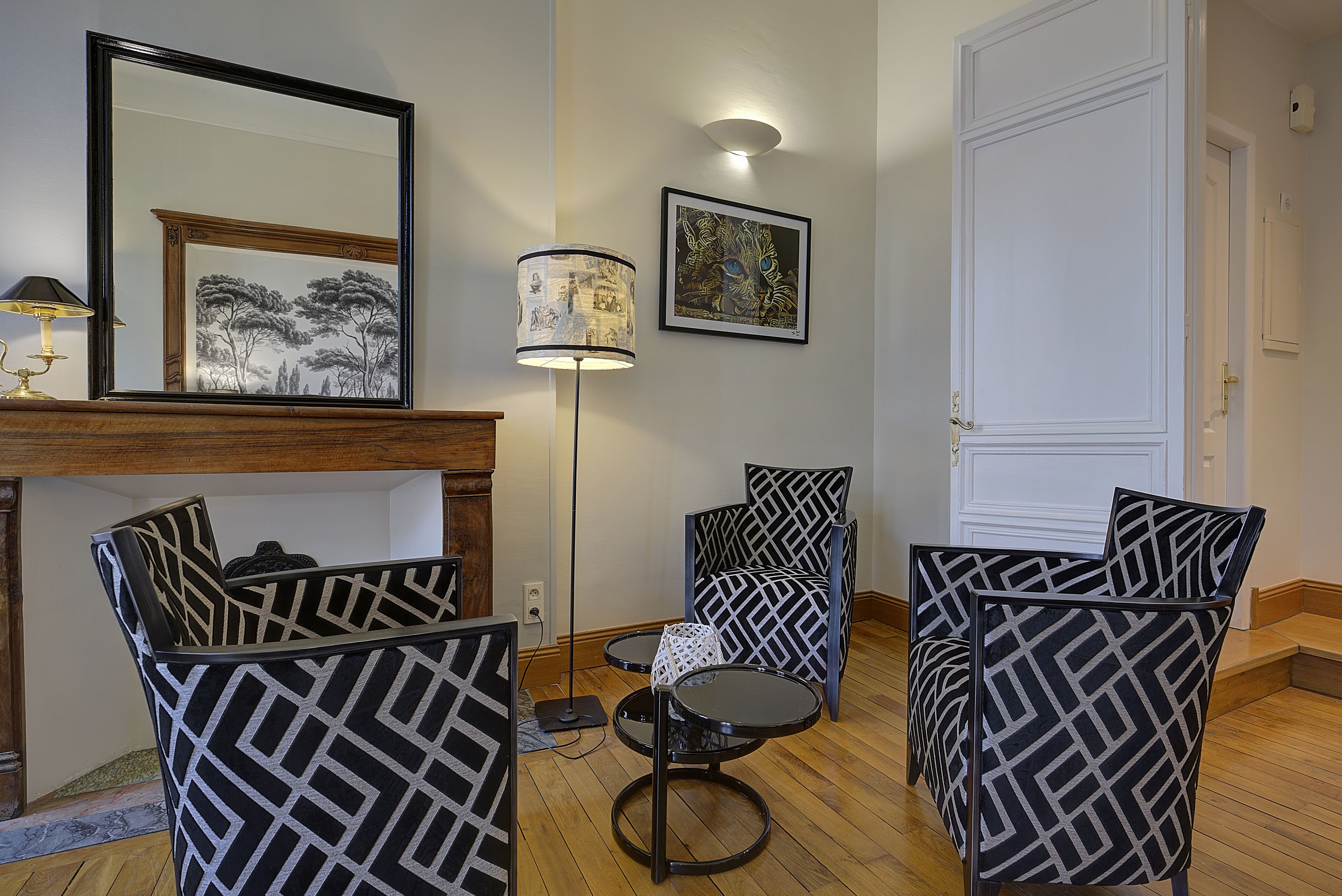 Un salon avec des fauteuils à motifs, une petite table, un lampadaire et une cheminée.