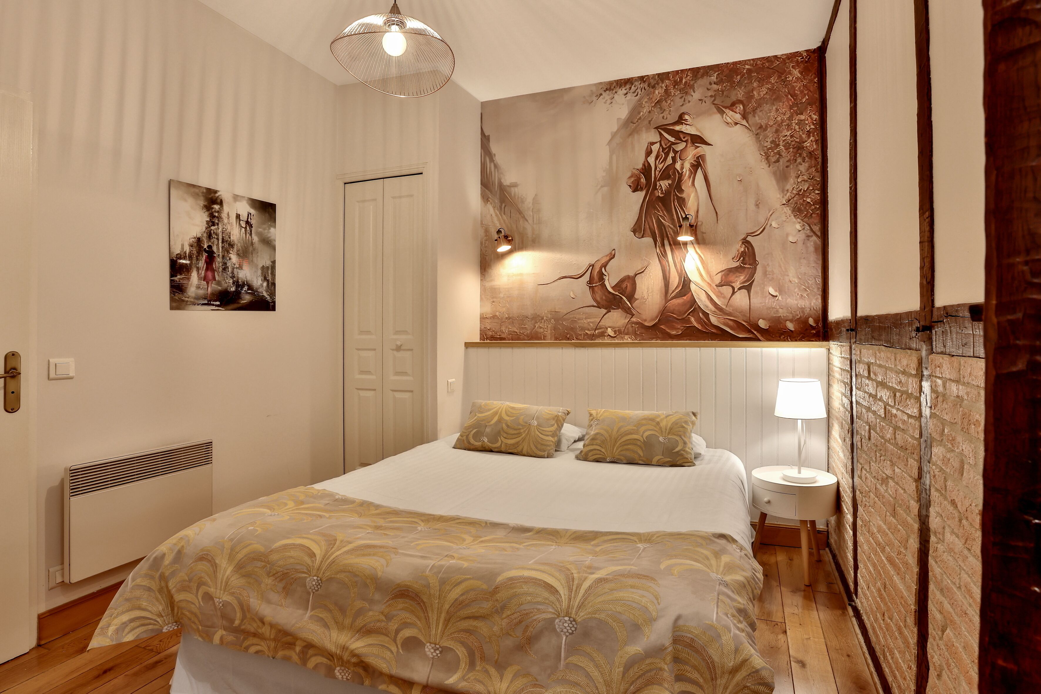 Een slaapkamer met een groot bed, een kunstwerk aan de muur, een nachtkastje met een lamp en een radiator.